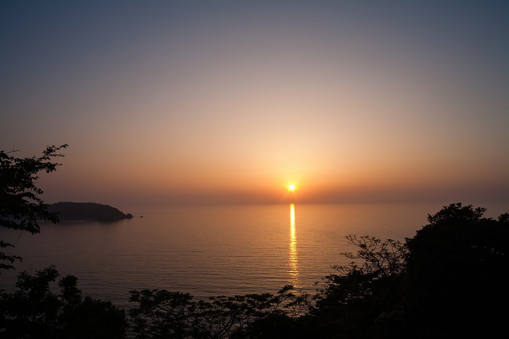 黄砂の中の水平線へ日没。