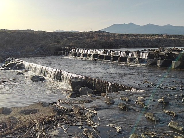岸辺から見えた川の堰と山並み